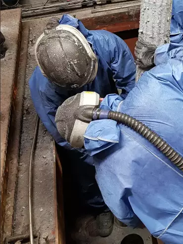 Opérateur portant un masque ventilé dans une atmosphère difficile, procédant au remplacement d’une manche filtrante dans un système de filtration industrielle.