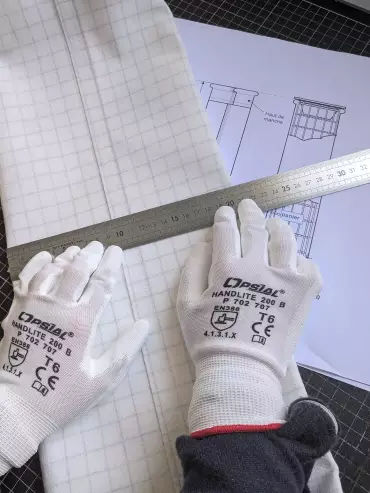Technicien en bureau d’étude mesurant une manche filtrante pour un système de dépoussiérage industriel.